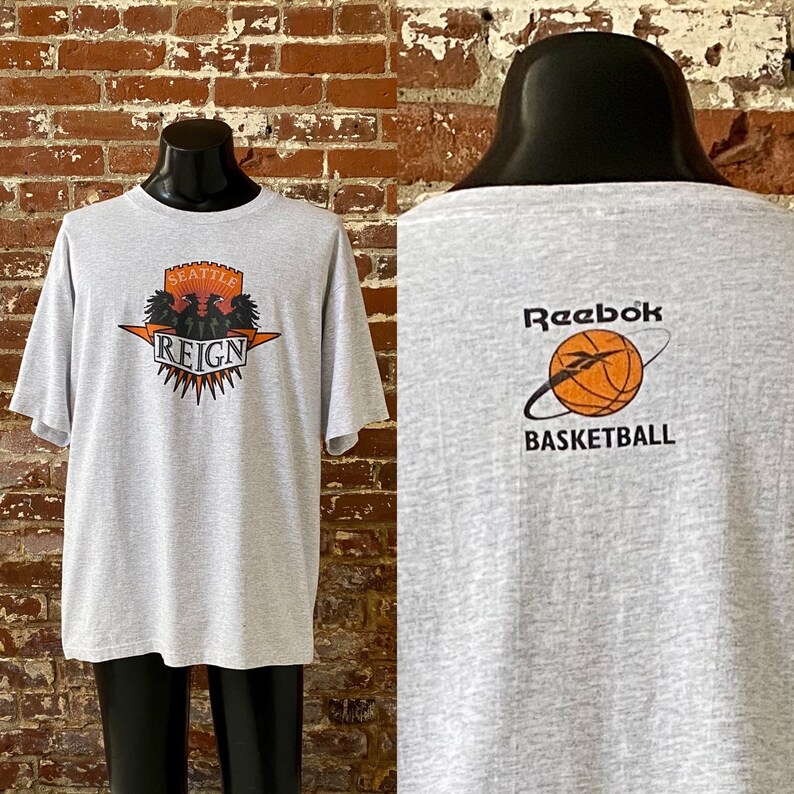 May include: Gray t-shirt with a Seattle Reign logo on the front and a Reebok Basketball logo on the back.
