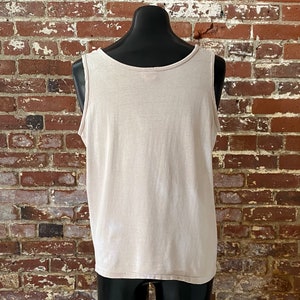 May include: A plain, light beige sleeveless shirt on a mannequin. The shirt is made of a soft, lightweight fabric.