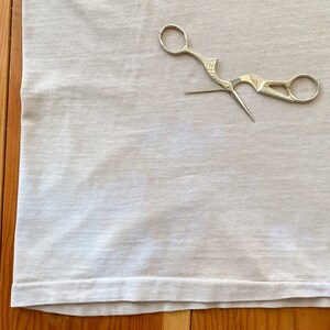 May include: A white fabric with a pair of silver scissors with a bird-like design on the handle.