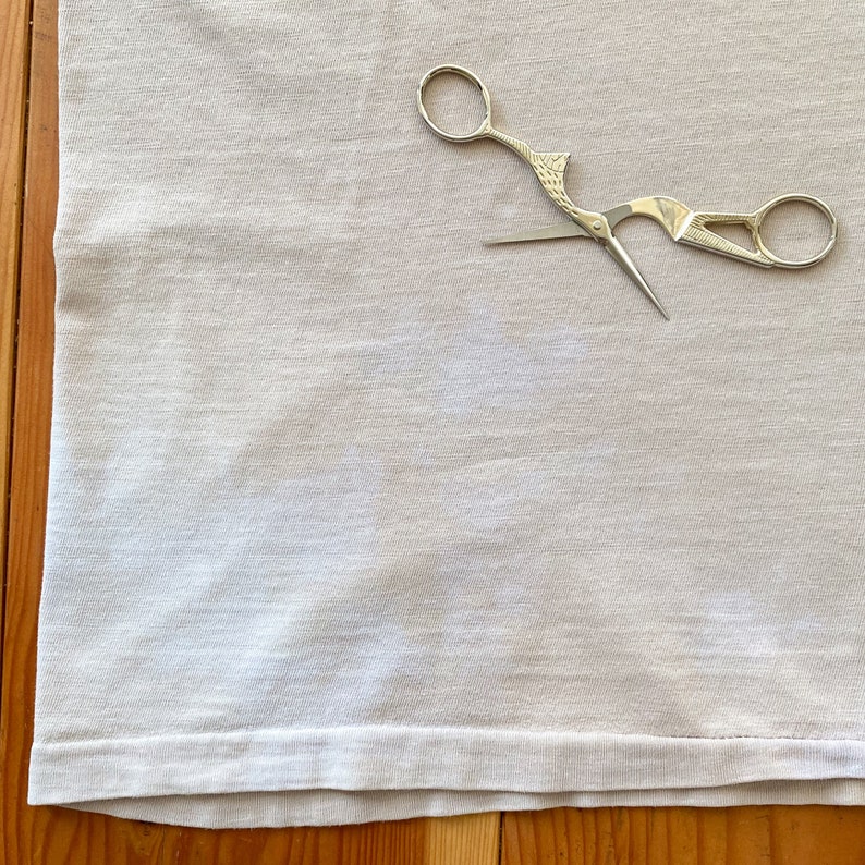 May include: A white fabric with a pair of silver scissors with a bird-like design on the handle.