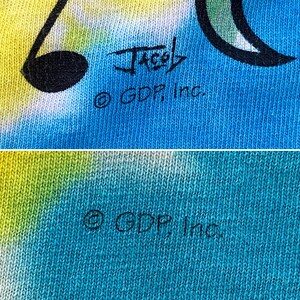 Op de afbeelding: Een close-up van een blauwe en groene tie-dye stof met de tekst "Jacob &copy; GDP, Inc." gedrukt in zwart.