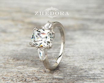 Pode incluir: Um anel de noivado de prata com um grande diamante quadrado e dois diamantes menores em forma de baguette de cada lado.