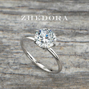 Può includere: Un anello di fidanzamento solitario con un diamante rotondo brillante incastonato in una fascia semplice ed elegante. L'anello è in oro bianco e presenta una montatura a sei griffe.