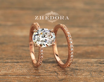 May include: Rose gold engagement ring set with an oval-shaped center stone and a matching band with pave diamonds. The set is on a wooden surface.