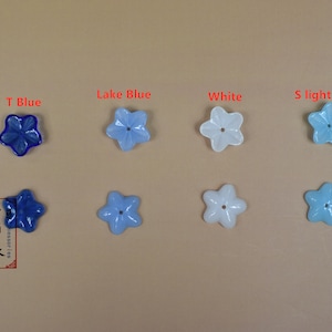 May include: Eight star-shaped glass beads in various shades of blue and white. The beads are arranged in two rows of four. The top row is labeled "T Blue", "Lake Blue", "White", and "S Light Blue".