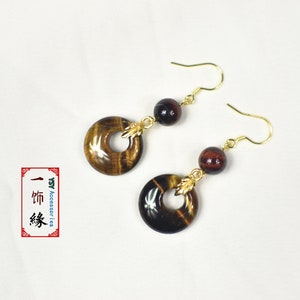 May include: A pair of gold dangle earrings with tiger's eye stone beads and round tiger's eye stone charms. The charms have a gold leaf design.