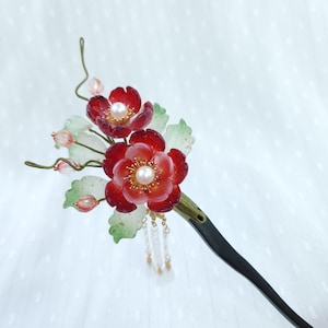 May include: A dark hair stick featuring two deep red translucent flowers with central white pearls, accented by pale green leaves, small pink beads on thin wire stems, and a cluster of dangling white beads attached to the base of the floral arrangement.