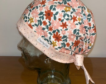 May include: A pink and white floral scrub hat with a pink and white polka dot tie. The hat has a label that says "Crafty Cole".