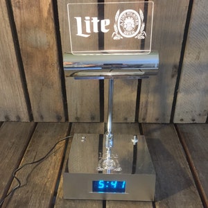 May include: A chrome desk lamp with a clear acrylic sign that reads "Lite" and a Miller Lite logo. The lamp has a digital clock that displays 5:41.