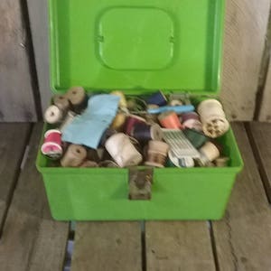 May include: A green plastic storage box filled with spools of thread, fabric scraps, and other sewing supplies.