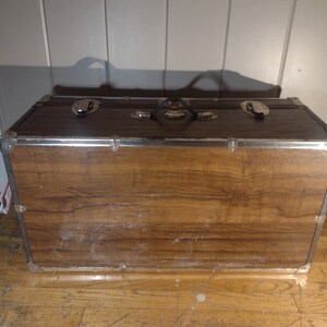May include: A brown wooden storage trunk with metal accents and a black handle. The trunk has a wood grain pattern and is closed.