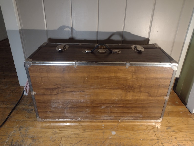 May include: A brown wooden storage trunk with metal accents and a black handle. The trunk has a wood grain pattern and is closed.
