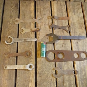 May include: A collection of vintage wrenches and a bottle opener on a wooden surface. The wrenches are made of metal and have a variety of sizes. The bottle opener is made of metal and has a rusty finish.