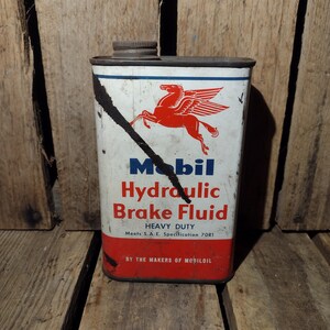 May include: Vintage Mobil Hydraulic Brake Fluid can with a red winged horse logo. The can is white with blue and red lettering. It says "Mobil Hydraulic Brake Fluid, Heavy Duty, Meets S.A.E. Specification 70R1, By the Makers of Mobiloil."
