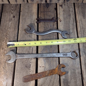 Puede incluir: Cuatro llaves inglesas sobre una superficie de madera. Las llaves inglesas son de metal y tienen diferentes tamaños. Una llave inglesa está oxidada. Las llaves inglesas están etiquetadas con los tamaños 15/16 y 1/2.