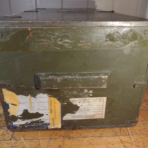 May include: A vintage green wooden storage box with a metal handle and a yellow shipping label. The label has the text "SHIPPING LABEL" and "NECESSARY" printed on it.