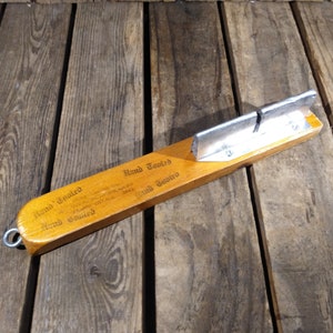May include: A wooden tool with a metal blade, labeled "Hand Tooled" and "Hand Tooled" with a small metal loop on the end.