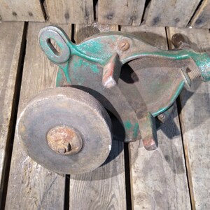 May include: A vintage green cast iron hand-crank sharpening tool with a round gray stone wheel. The tool has a metal handle and a threaded rod for adjusting the stone.