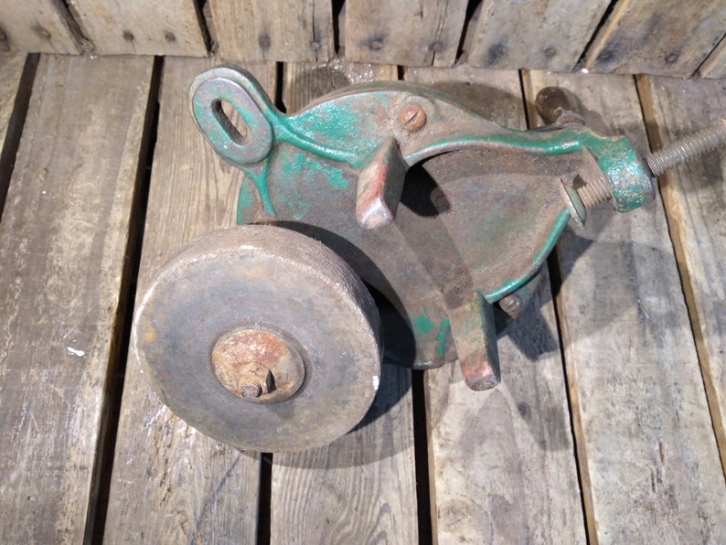 May include: A vintage green cast iron hand-crank sharpening tool with a round gray stone wheel. The tool has a metal handle and a threaded rod for adjusting the stone.