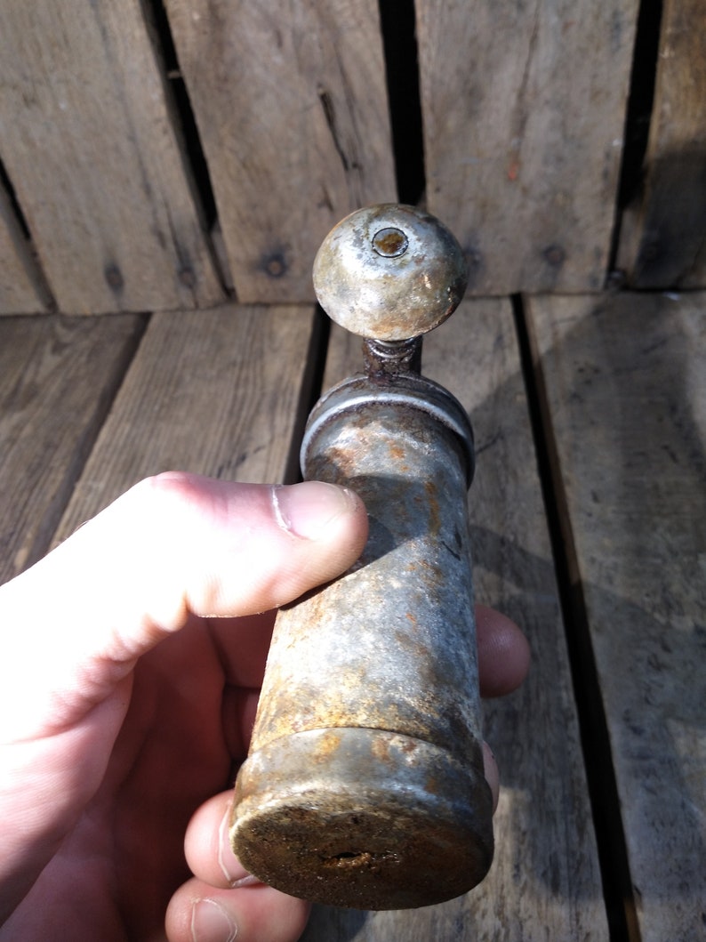 May include: A vintage metal pepper grinder with a round top and a cylindrical body. The grinder is silver with rust spots and has a small hole at the bottom.