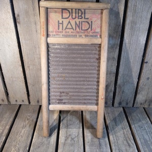 Op de afbeelding: Een vintage houten wasbord met een gegolfd metalen oppervlak. Het wasbord heeft een label met de tekst "Duble Handi" en "Columbus Washboard Co., Columbus, O."