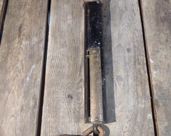 May include: A black and silver hanging scale with a hook on one end and a ring on the other. The scale has a numbered dial for measuring weight.