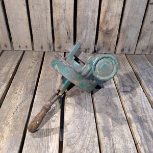 May include: A green metal pipe cutter with a wooden handle. The cutter is lying on a wooden surface.