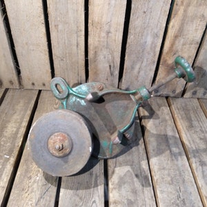 May include: A vintage green metal hand-crank sharpening tool with a round gray grinding wheel. The tool is made of cast iron and has a wooden handle.