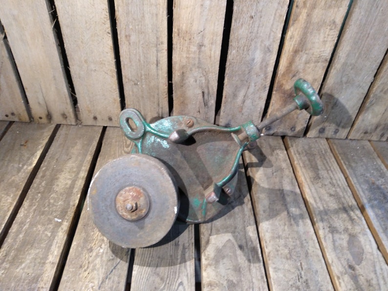 May include: A vintage green metal hand-crank sharpening tool with a round gray grinding wheel. The tool is made of cast iron and has a wooden handle.
