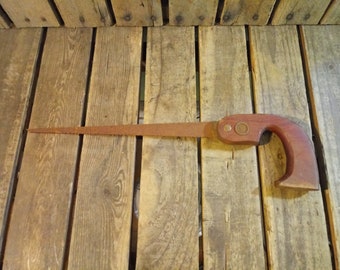 May include: A vintage hand saw with a wooden handle. The saw blade is rusty and the handle is worn. The saw is lying on a wooden surface.