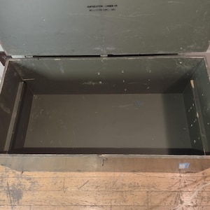 May include: A large, green wooden storage chest with a hinged lid. The chest is empty and the inside is visible. The chest is made of wood and has a metal latch.