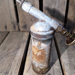 May include: A rusty, silver-colored grease gun with a long nozzle and a spring-loaded plunger. The grease gun is labeled "N274172".