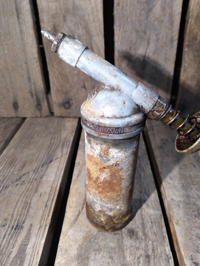 May include: A rusty, silver-colored grease gun with a long nozzle and a spring-loaded plunger. The grease gun is labeled "N274172".
