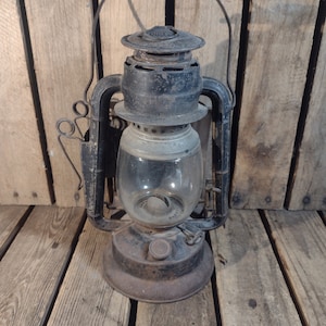May include: A vintage black kerosene lantern with a glass globe and a metal handle. The lantern has a worn, rustic look and is sitting on a wooden surface.