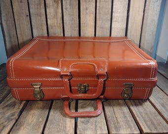 May include: A vintage brown leather suitcase with brass hardware and white stitching. The suitcase has a handle and two clasps.