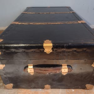 Puede incluir: Ba&uacute;l de equipaje vintage negro con detalles dorados y asa de cuero.