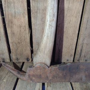 May include: A rusty, antique axe with a wooden handle. The axe is resting on a wooden surface.
