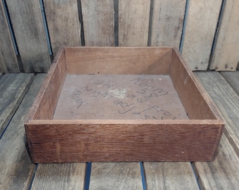 May include: A rectangular wooden box with a dark brown finish. The box has a simple, open design and appears to be handmade. The interior base of the box has handwritten text. The box is sitting on a wooden surface.