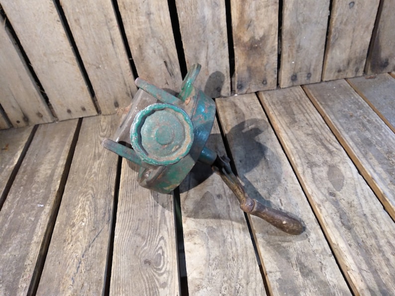 May include: A vintage green metal hand crank with a wooden handle. The crank has a large, round, green metal knob.