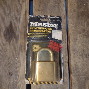 May include: A gold-colored combination padlock with the words "Master" and "Set-Your-Own Combination" on the packaging. The padlock has a black and yellow warning label that says "Maximum Security".