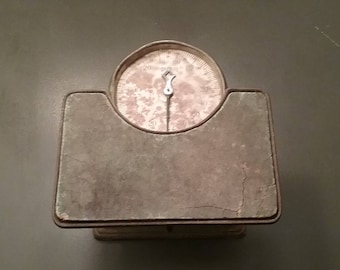 May include: A vintage, silver-colored, analog scale with a round face and a single hand. The scale is made of metal and has a worn, aged appearance.