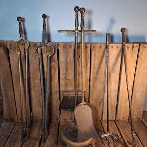 May include: A set of fireplace tools including a pair of tongs, a poker, a shovel, a brush, and a rake, all featuring long metal handles with spherical finials. The tools are arranged upright, with the shovel and brush resting on a circular base.