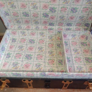 Puede incluir: Un ba&uacute;l de madera vintage con herrajes de lat&oacute;n y un forro con estampado floral. El ba&uacute;l tiene un peque&ntilde;o compartimento en el interior.