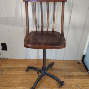 May include: A vintage wooden chair with a slatted back and a swivel base with cast iron wheels. The chair is made of dark wood and has a worn finish.