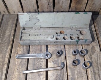 May include: A metal tool box with a hinged lid, containing a set of sockets and a wrench. The box is labeled with the sizes of the sockets: 9/16, 5/8, 3/4, 7/8, and 15/16. The box is sitting on a wooden surface.