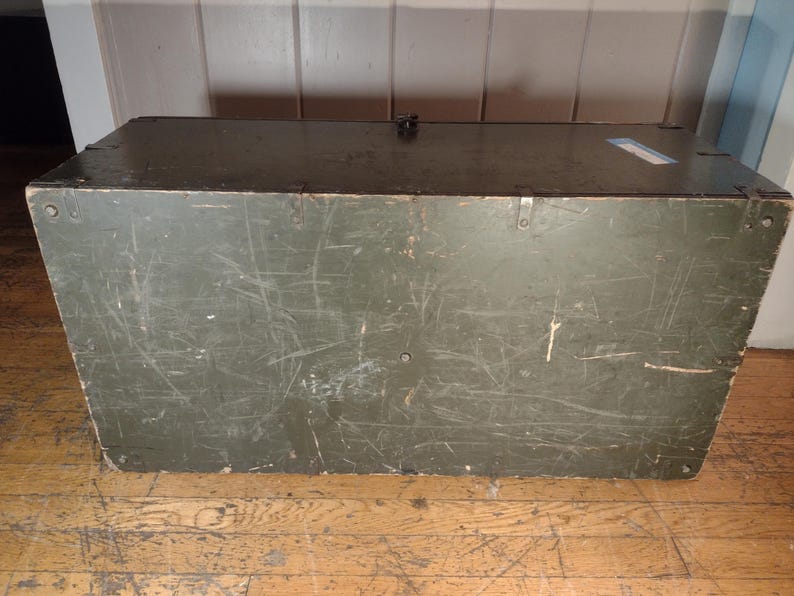 May include: A vintage green wooden storage chest with metal clasps and a worn surface. The chest has a dark green paint finish and shows signs of age and use.
