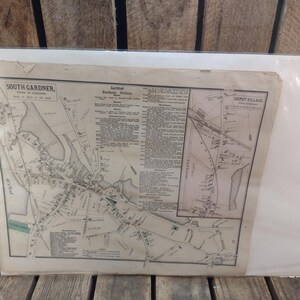 May include: An antique map of South Gardner, Massachusetts, featuring detailed street layouts, labeled landmarks, and text. The map is encased in a protective plastic sleeve, with visible text including "Depot Village" and "Gardner Business Directory".