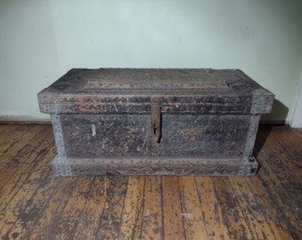 Puede incluir: Un gran cofre de madera oscura con detalles metálicos y una tapa con bisagras. El cofre está desgastado y muestra signos de la edad. Tiene un pestillo y bisagras de metal.