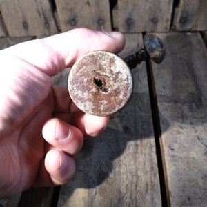 May include: Close-up of the bottom of a vintage, rusty, metal bottle opener with a wooden handle. The handle has a hole in the center.