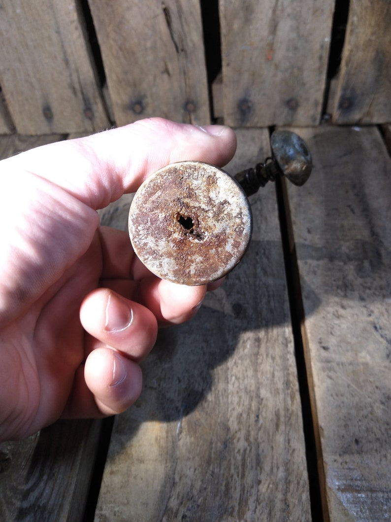 May include: Close-up of the bottom of a vintage, rusty, metal bottle opener with a wooden handle. The handle has a hole in the center.